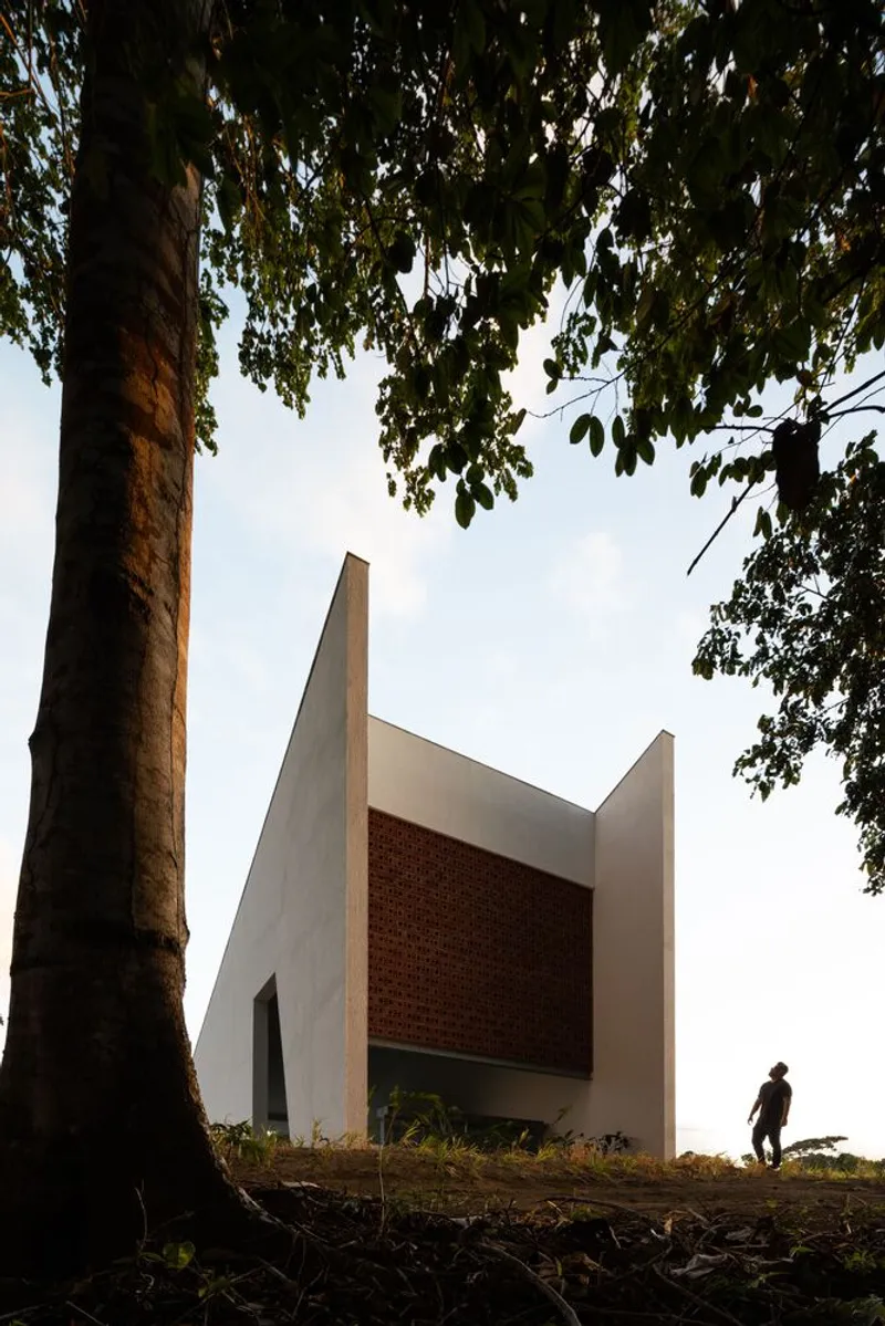 White geometric facade with brick panel seen through tree trunks with a figure walking near