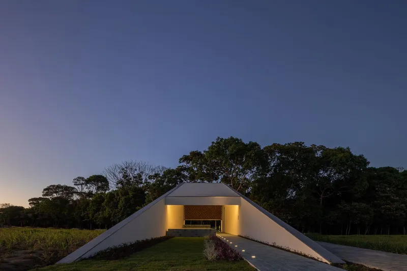 White arched pavilion with illuminated brick wall and grassy approach at twilight beneath a clearing sky