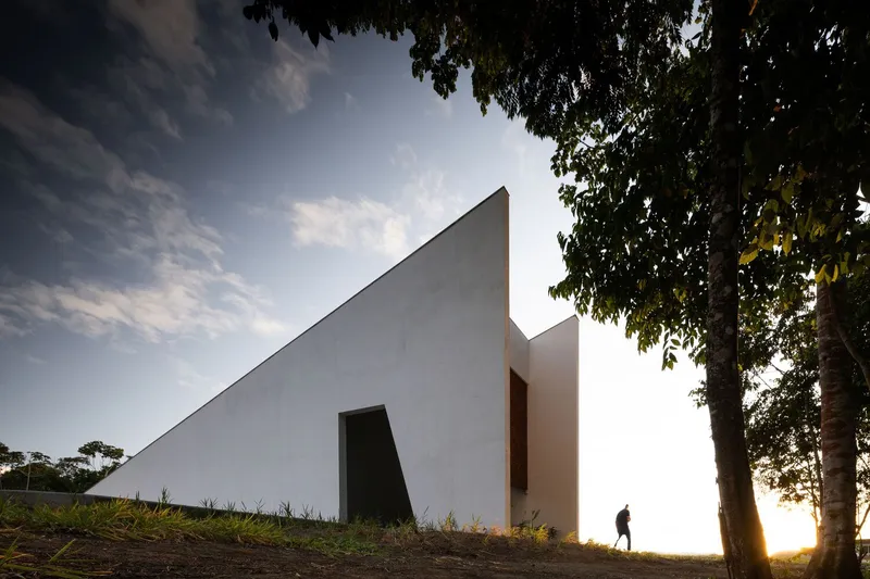Sloping white wall with recessed opening at golden hour with figure walking in backlit grass