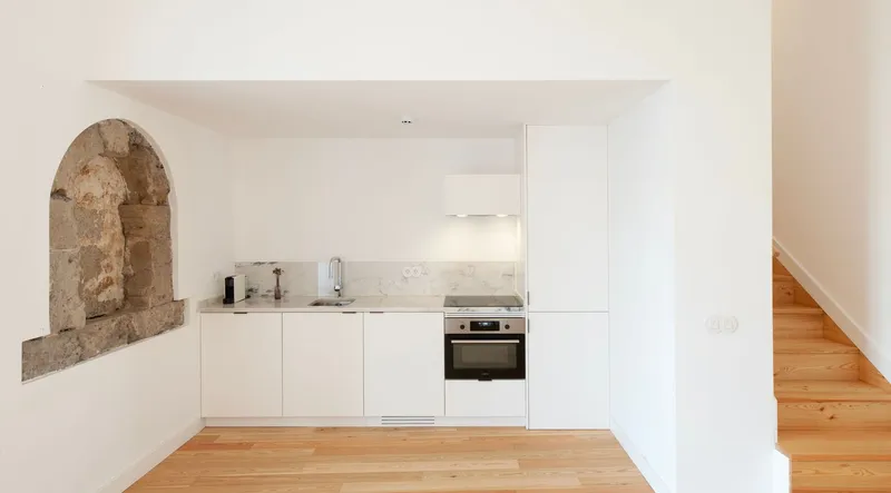 White kitchen with exposed stone arch niche and light wood flooring beneath a white ceiling