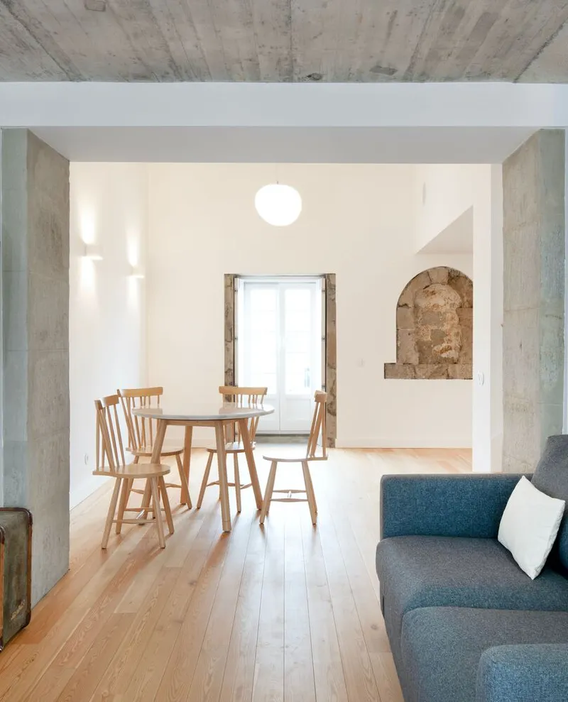 Open living space framed by concrete columns with exposed stone niche and wood dining furniture