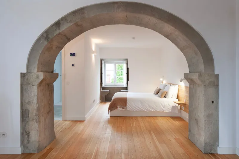 Bedroom viewed through a preserved stone archway with light wood flooring and white plastered walls