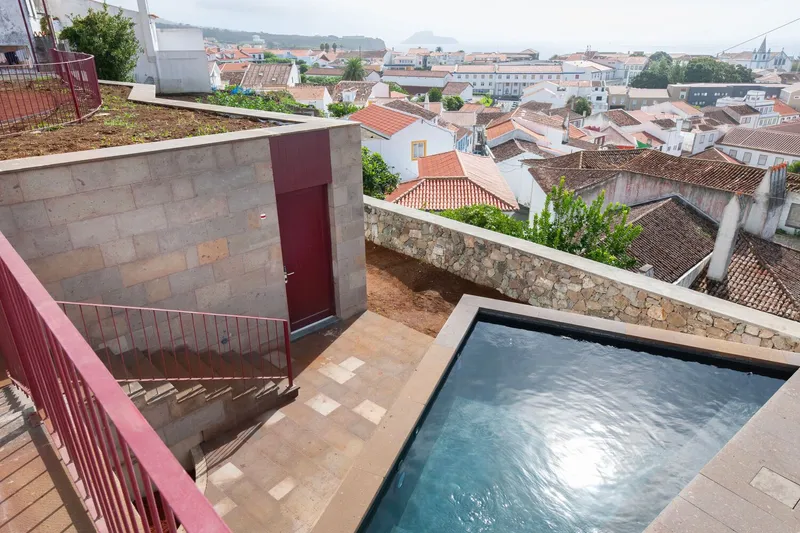 Rooftop terrace with rectangular pool and concrete volume overlooking terracotta rooftops under overcast sky