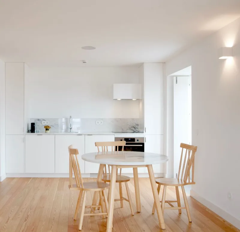 Open kitchen with white cabinetry and marble backsplash adjoining a dining area with light wood chairs