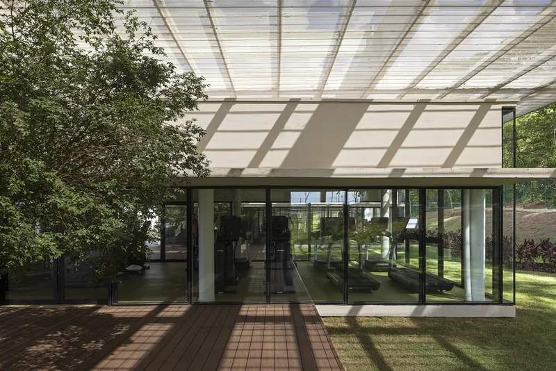 Glazed entrance facade beneath a translucent canopy with timber decking casting strong shadows in afternoon light