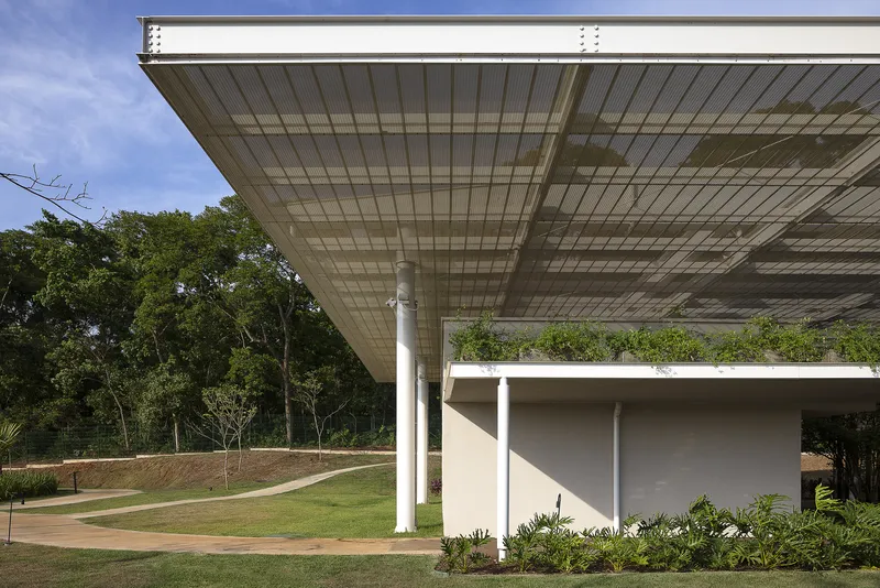 Wide cantilevered roof with translucent panels supported by white columns above a planted garden bed
