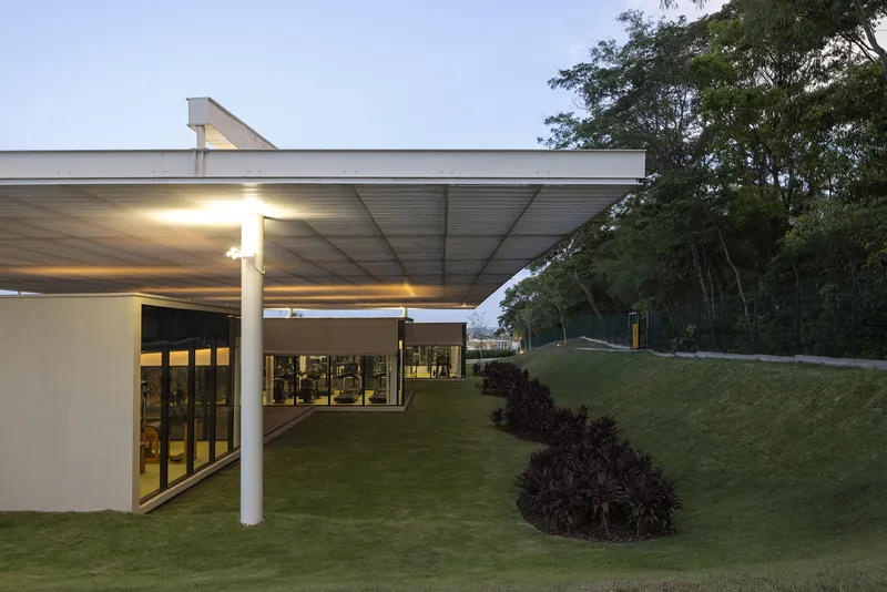 Illuminated covered terrace with glass walls and sculptural planted mounds at dusk