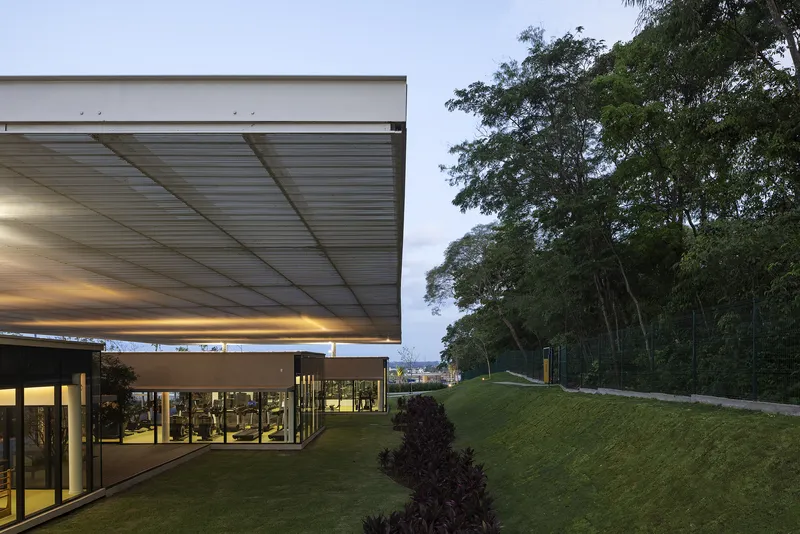 Cantilevered roof edge at twilight with lit interior spaces visible through the glazed facade