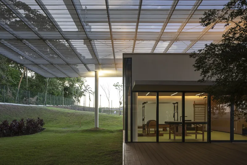 Covered terrace with louvered canopy and glass-walled fitness room at twilight