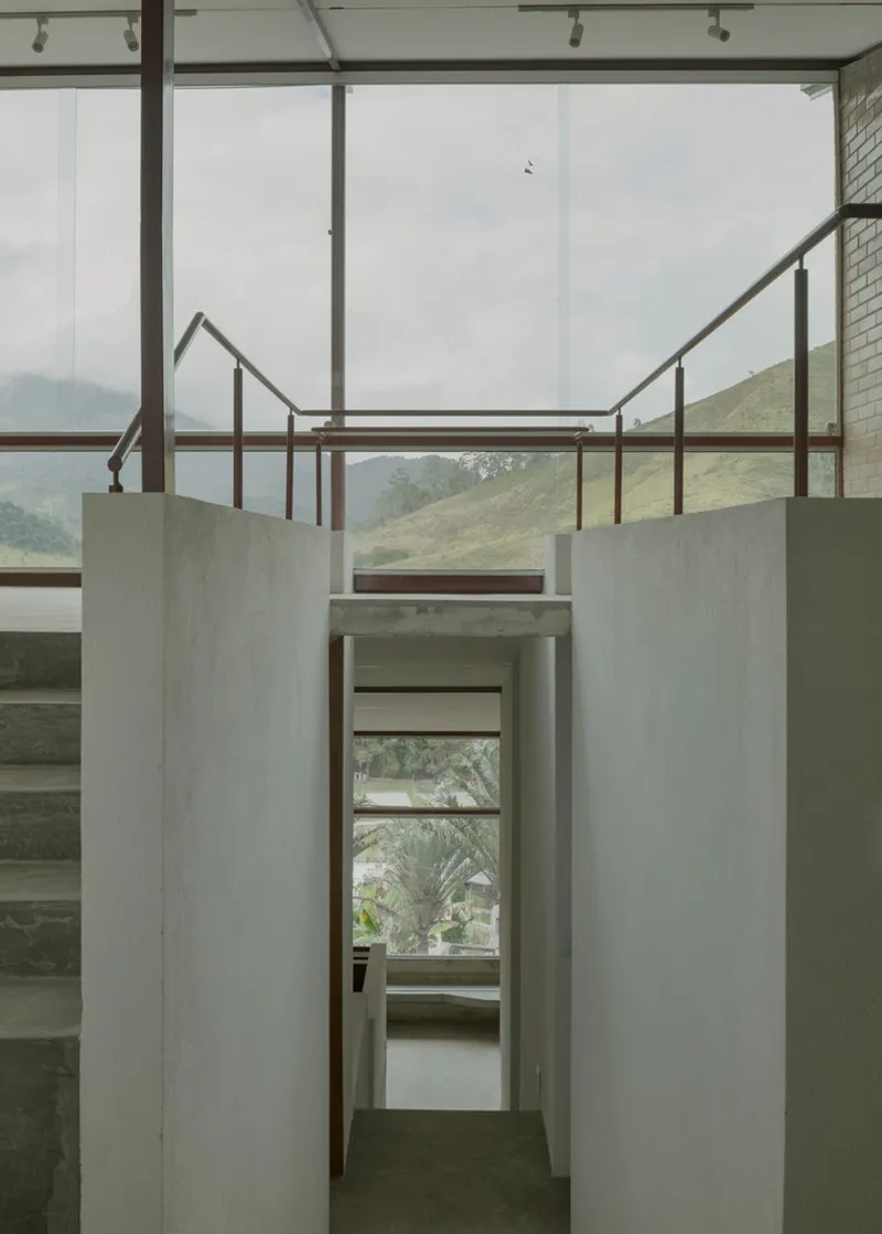 Concrete-walled corridor with steel-framed glazing above and view through to mezzanine under overcast sky