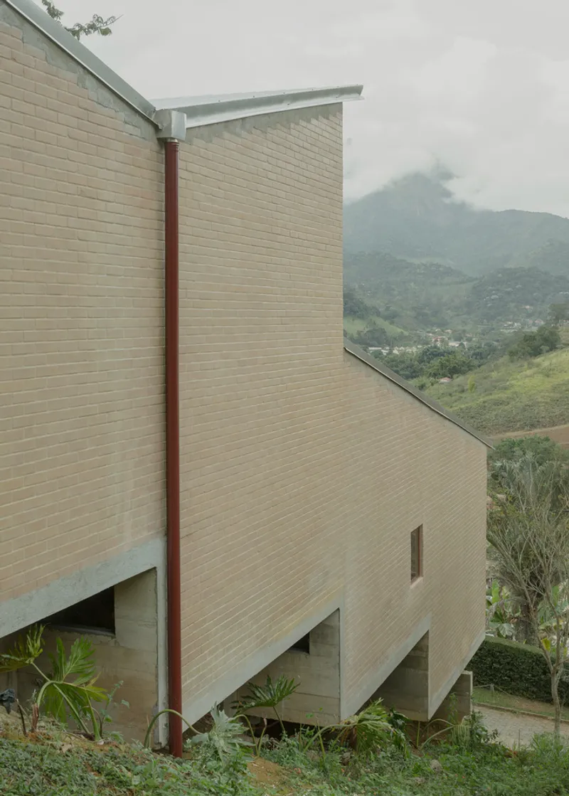 Cantilevered tan brick volumes with metal column framing misty mountain views in the background