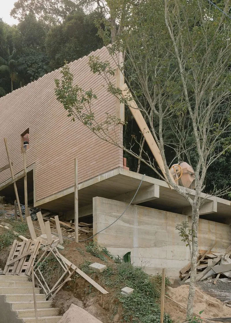 Angled corrugated roof volume on concrete supports surrounded by young trees amid construction debris