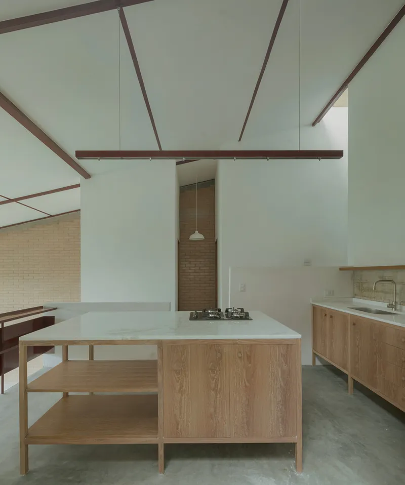 Kitchen island with timber shelving and white countertop beneath red steel beams and a double-height ceiling