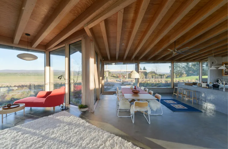 Open-plan living space with exposed timber joists and floor-to-ceiling glazing overlooking pastoral fields