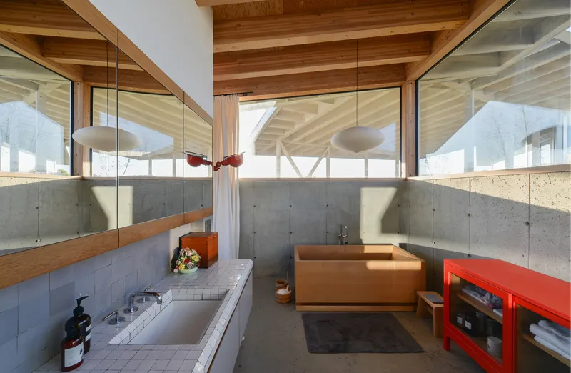 Bathroom with concrete half-walls, timber ceiling, and clerestory windows filtering afternoon sunlight