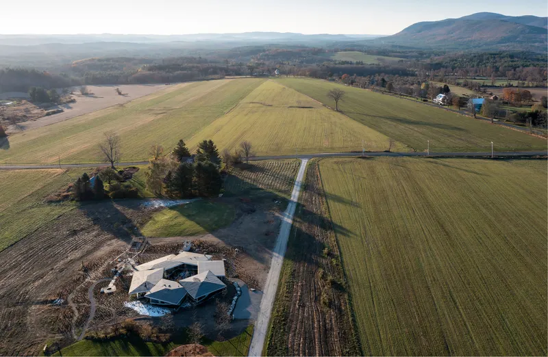 Aerial view of the angular glass residence surrounded by cultivated fields and distant mountains