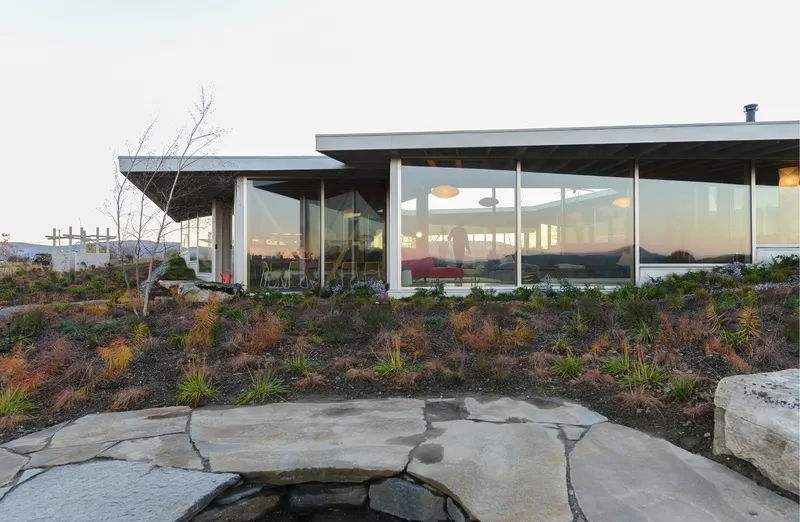 Flagstone patio with young plantings leading to the glass-walled living room at dusk