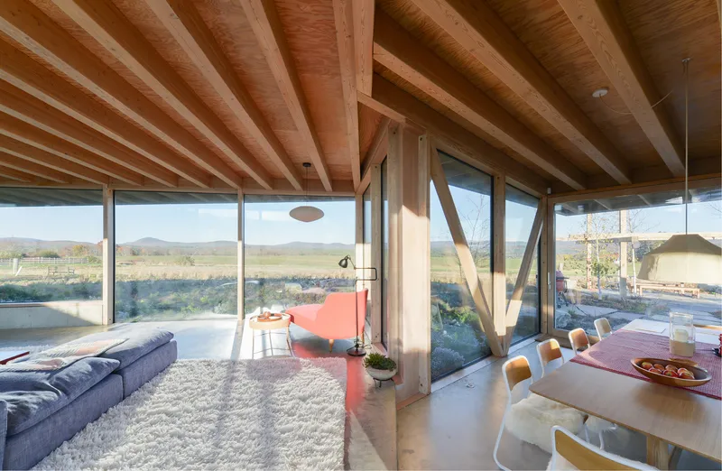 Open-plan living and dining space with exposed timber beams and full-height glazing overlooking landscape