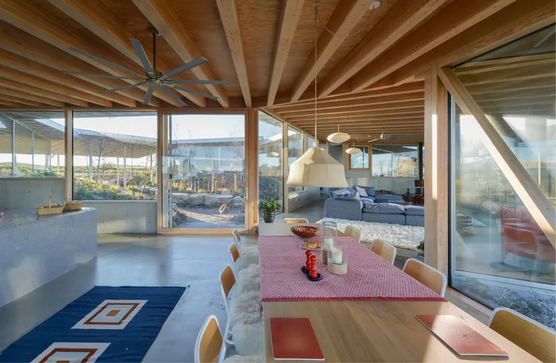Dining area with timber ceiling joists and angled structural bracing framing the glazed perimeter walls