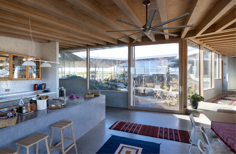 Kitchen island with concrete countertop beneath wood joist ceiling and corner glazing to courtyard