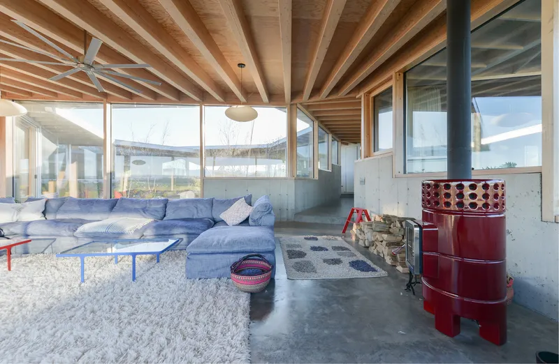 Seating area with red wood-burning stove and stacked firewood beside concrete partition wall