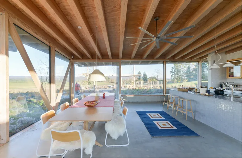 Open plan living and dining space with exposed timber beams and full-height glazing overlooking open fields