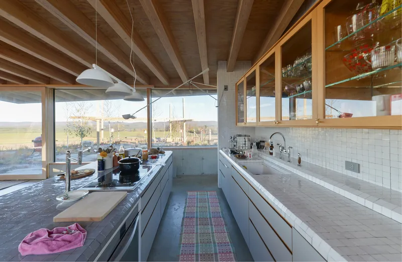 Galley kitchen with white tile backsplash and concrete countertops beneath exposed timber ceiling structure