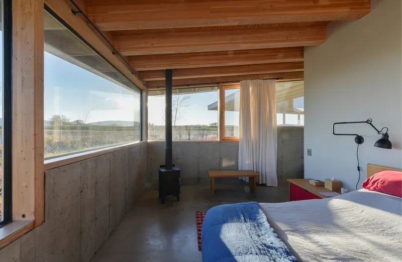 Bedroom with board-formed concrete half-walls and horizontal ribbon window framing distant hills