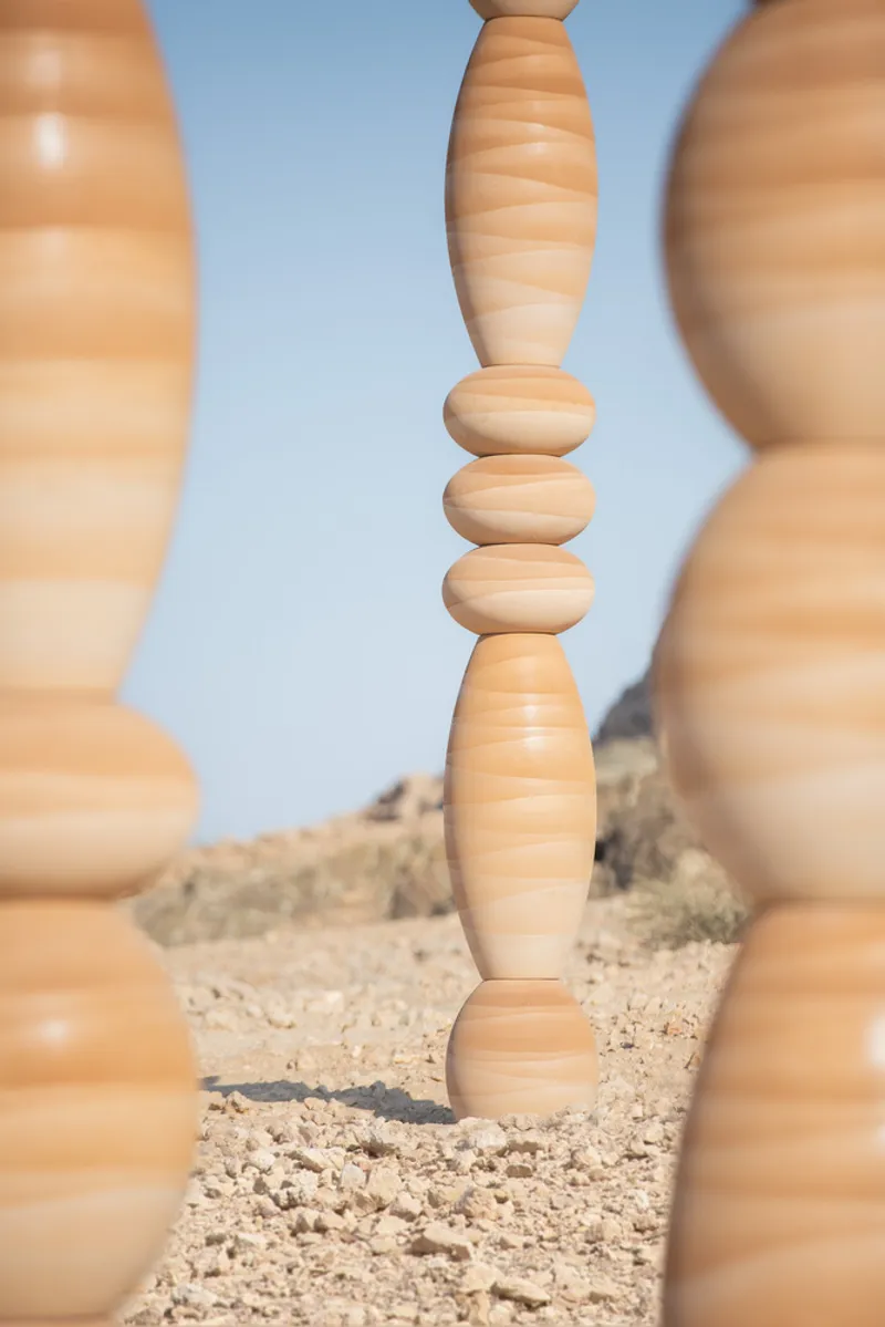 Close view through foreground columns showing the stacked spherical and elliptical segments of a central timber piece