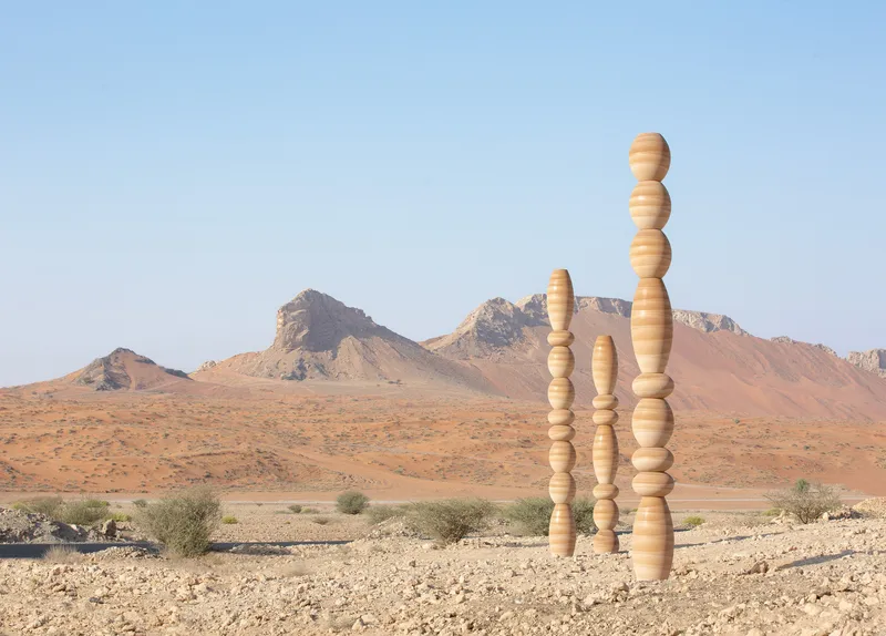 Cluster of vertically stacked timber spheres rising from the gravel terrain against distant mountains