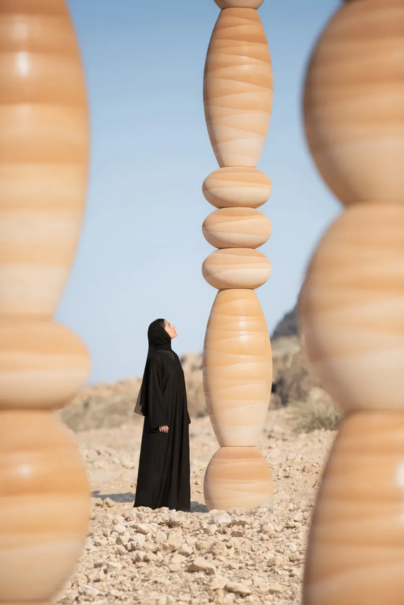 Figure in black robes framed between stacked wood columns with elliptical and spherical segments