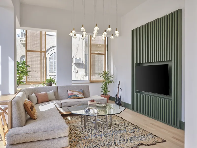 Living room with green vertical slat media wall and tall windows framing neighboring buildings