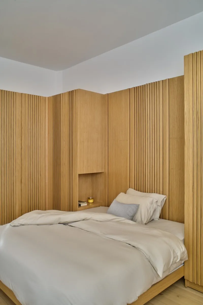 Bedroom corner with vertical oak slat wall panels wrapping around a recessed bed niche