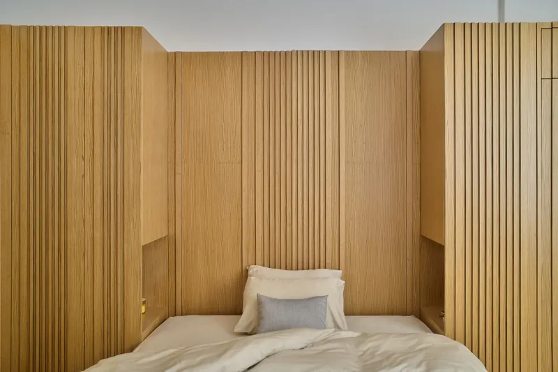 Bedroom niche with vertical timber slat walls and ceiling surrounding a bed in soft light
