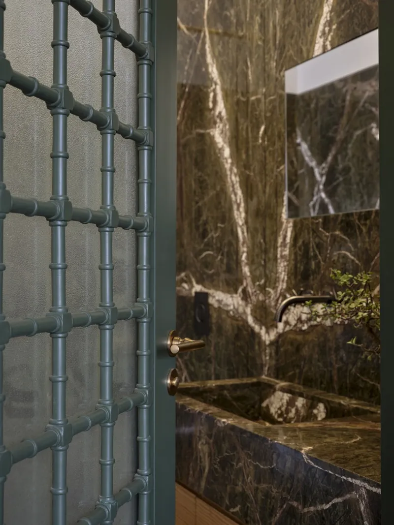 Bathroom doorway showing a green metal screen and dark marble walls around a stone basin
