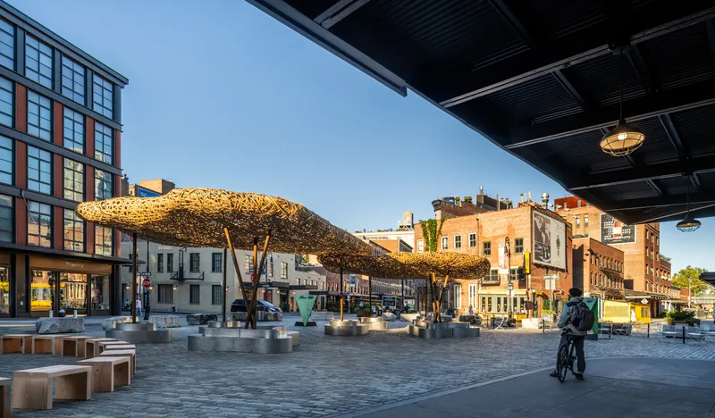 Long view of the clustered woven canopies in evening light with a cyclist crossing the plaza