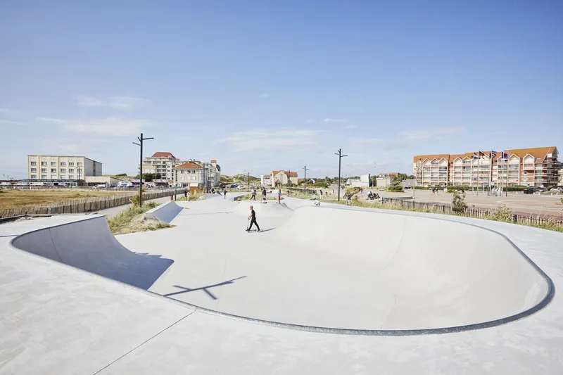 Oval concrete skating bowl with a person walking across its smooth surface in bright sun