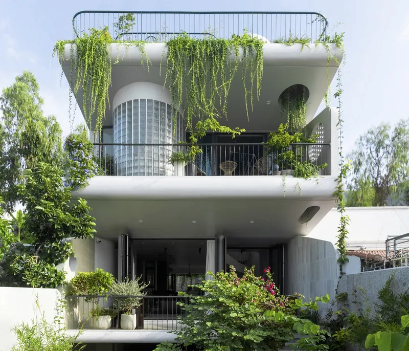 White curved balconies with cascading vines and glass block bay window framed by lush garden foliage