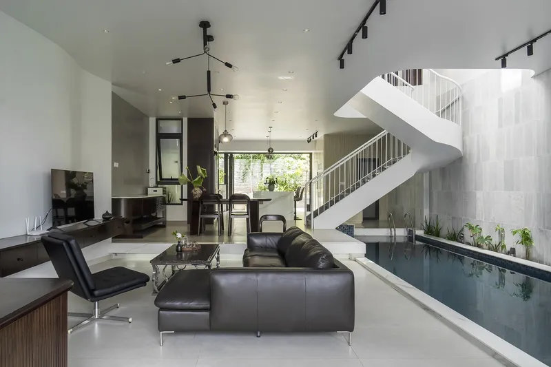 Open living space with white steel staircase rising above an interior lap pool