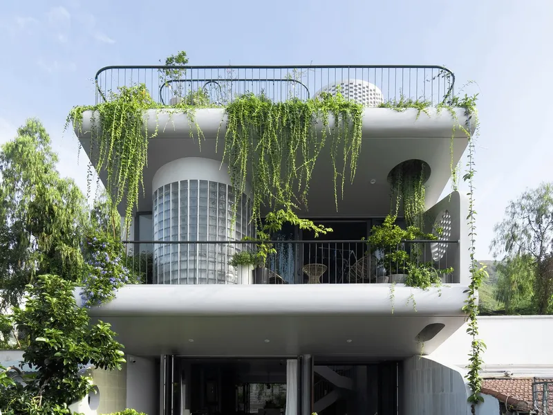 Front elevation showing curved balconies with hanging greenery and cylindrical glass block element under blue sky