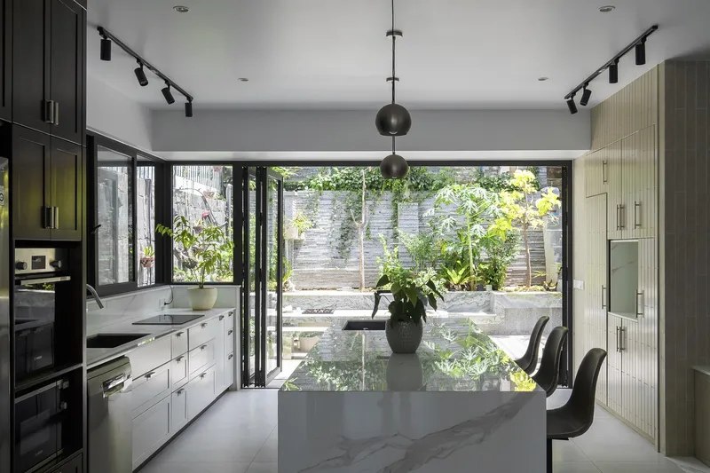 Kitchen with marble island looking through black-framed glass doors to a planted courtyard