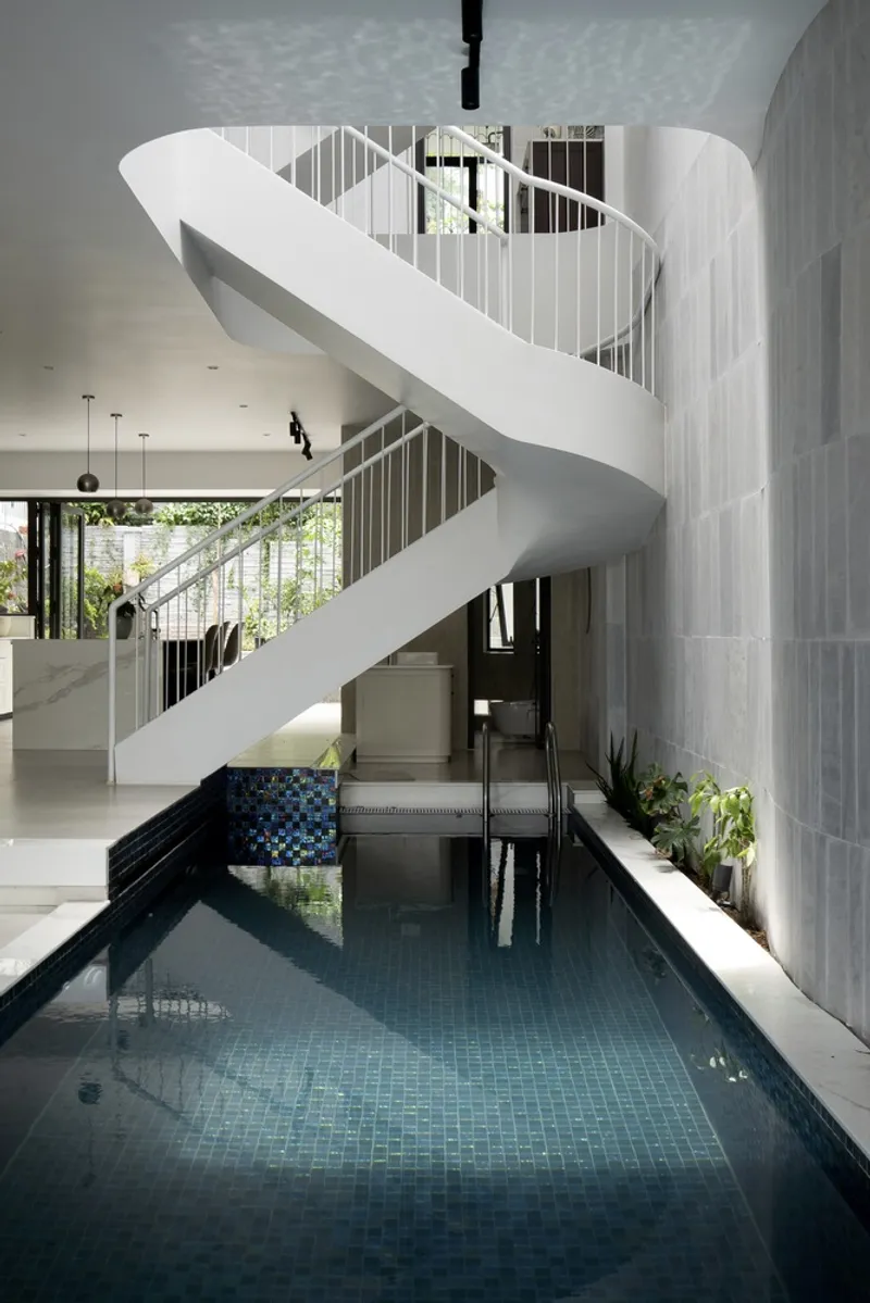 Helical white staircase rising above an indoor lap pool with dark tile and grey stone walls