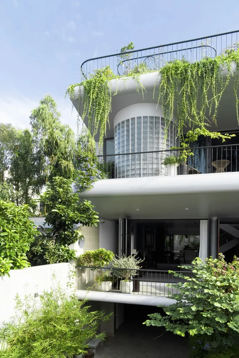 Stacked balconies with trailing vines and cylindrical glass block tower visible through surrounding trees