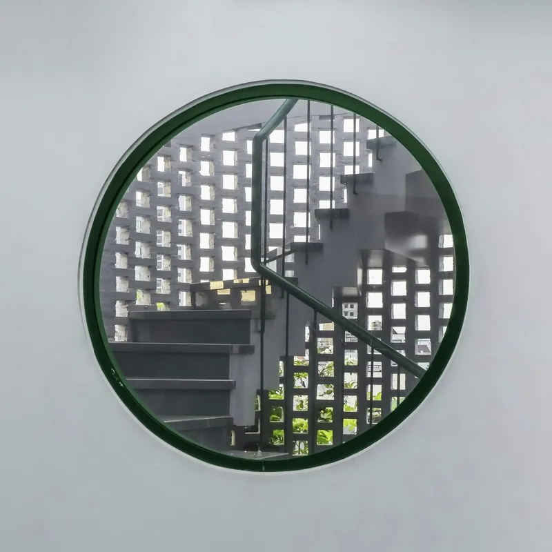 Circular window with dark green frame revealing a perforated brick screen and steel staircase beyond