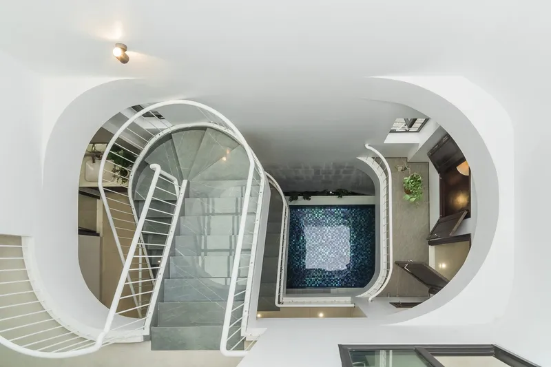 Top-down view through the curved double-height void showing the blue-tiled courtyard pool below