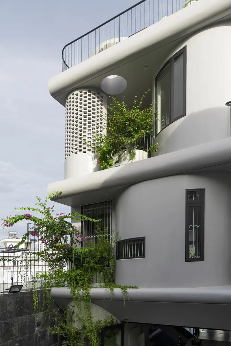White perforated cylindrical screens framing balconies planted with cascading greenery and flowering vines