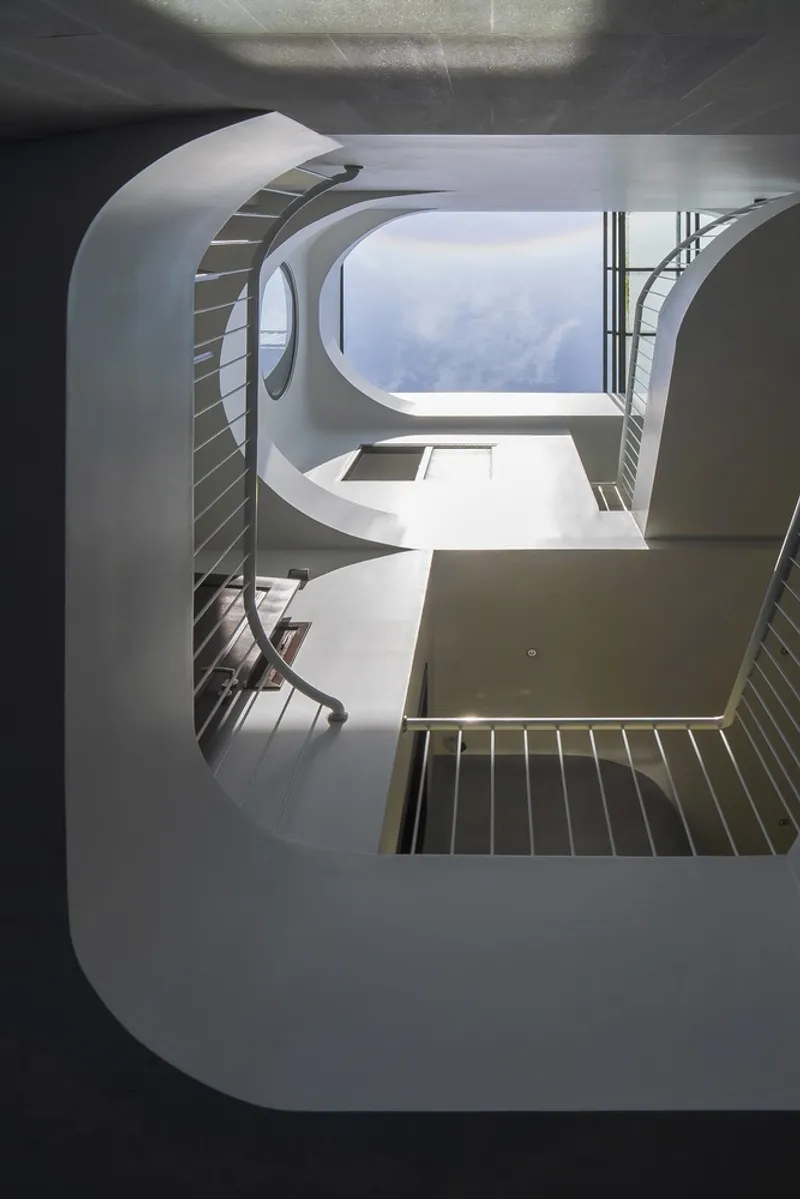 Upward view of the spiraling white staircase wrapping around a central void open to the sky