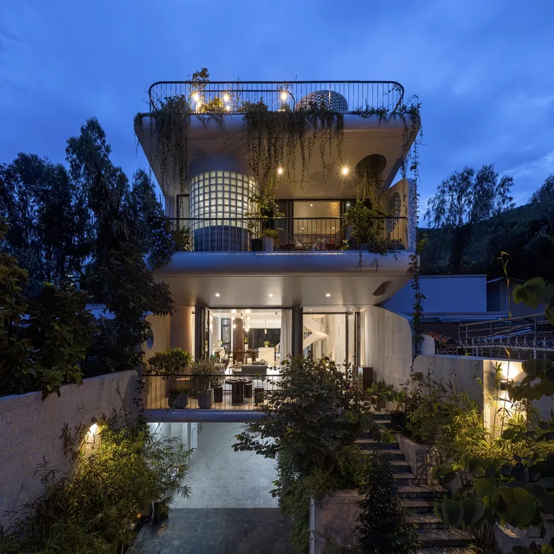 Illuminated facade at dusk with planted terraces draping vegetation over curved white balconies