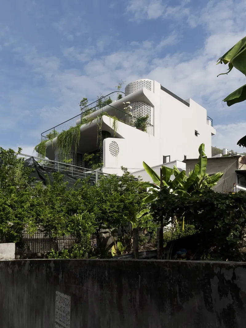 White facade with rounded balconies and perforated screens rising above banana trees and dense vegetation