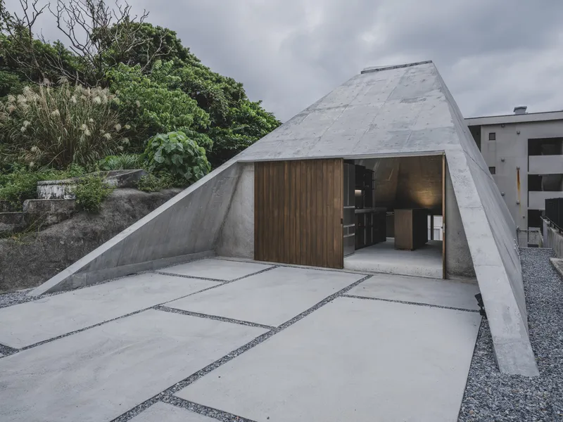 Entrance courtyard with concrete paving slabs set in gravel beneath a sloping concrete canopy